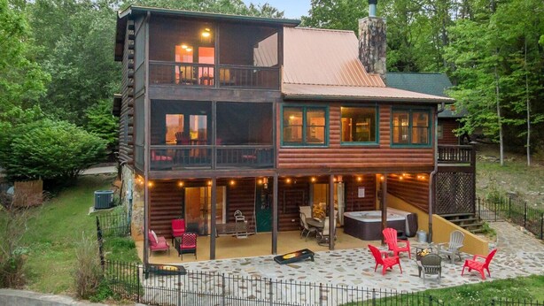 Une cabane en rondins à deux étages, dotée d’un balcon, d’un espace extérieur aménagé pour s’asseoir et d’une cheminée en pierre.