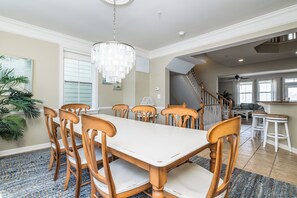 A dining area with a white table and wooden chairs, a chandelier, and a staircase leading to another room.