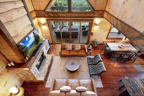 A spacious loft-style room with a stone fireplace, a large sofa, a dining table, and a view of the outdoors.