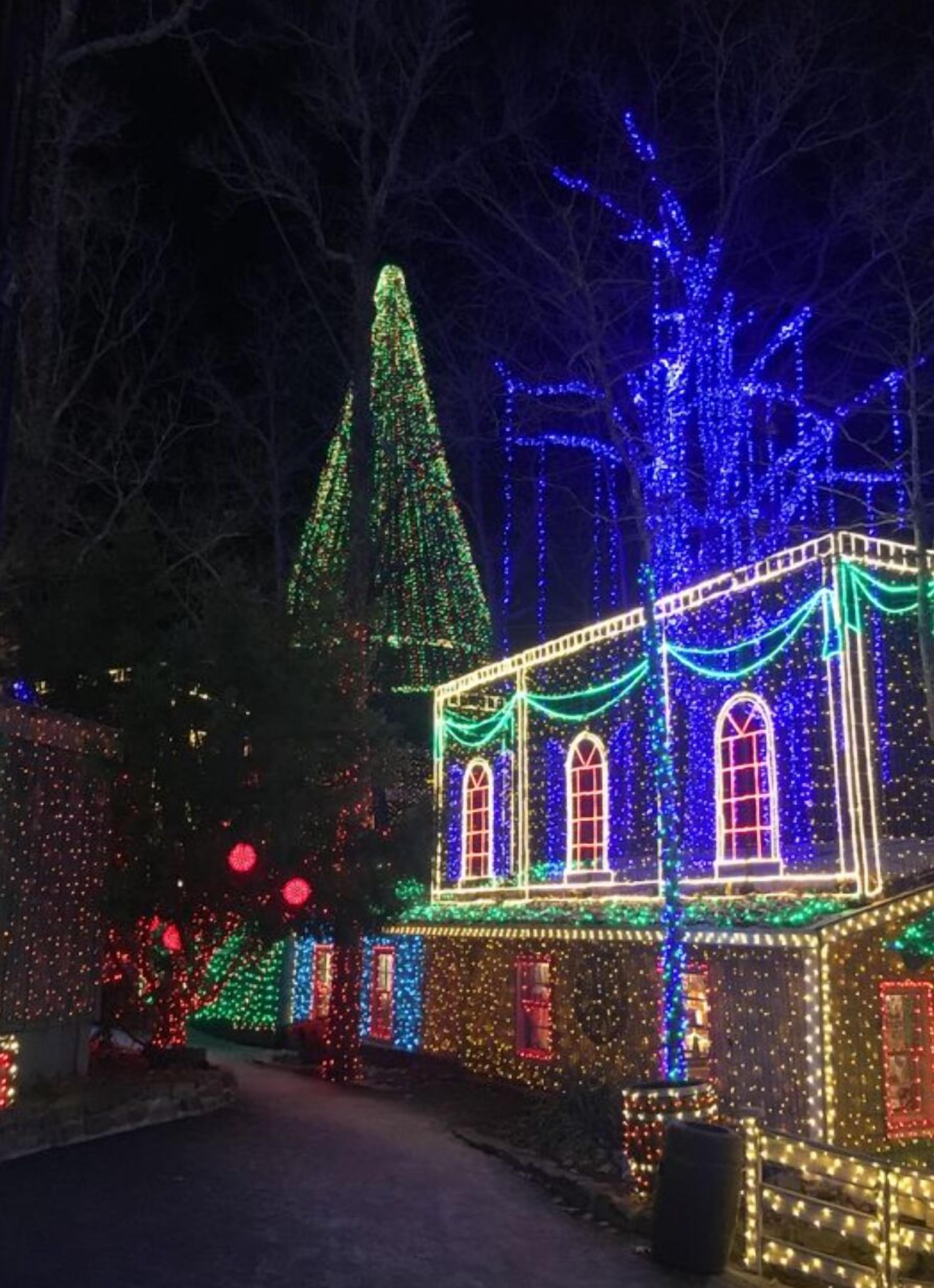 A building with a pointed roof and a large arched window, surrounded by trees and decorated with colorful lights.