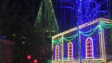 A building with a pointed roof and a large arched window, surrounded by trees and decorated with colorful lights.
