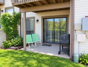 A covered patio with a grill, two chairs, and a sliding glass door leading to a backyard. - Clean Comfortable Condo with Golf Course View - Close to Pool & Clubhouse! (Branson)