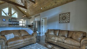 A spacious living room with two leather sofas, a wooden ceiling, and a kitchen in the background. - Serenity Now - Cherry Log (Cherry Log)