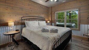 A bedroom with a bed, a ceiling fan, a window, and a nightstand with a lamp. - Serenity Now - Cherry Log (Cherry Log)