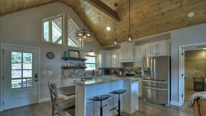 A spacious kitchen with wooden beams, a large island with bar stools, stainless steel appliances, and a view of the outdoors. - Serenity Now - Cherry Log (Cherry Log)