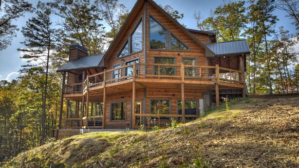 Eine große Holzhütte mit mehreren Balkonen und großen Fenstern, umgeben von Bäumen.