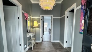 A hallway with a chandelier, a desk with a lamp, and a door with a decorative mirror. - Pollyanna Hunter Valley (Cessnock)