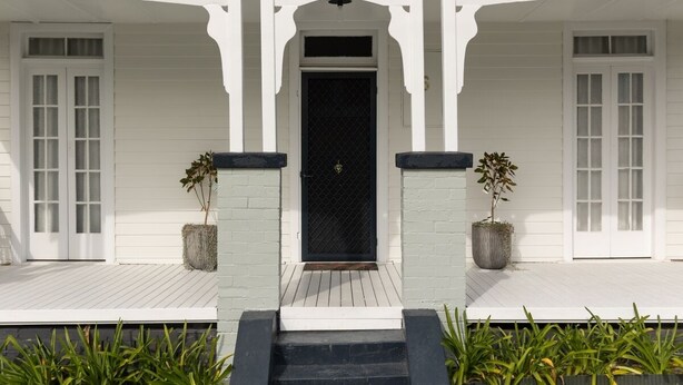 A white building with a black door, two potted plants, and a wooden deck. - Pollyanna Hunter Valley (Cessnock)