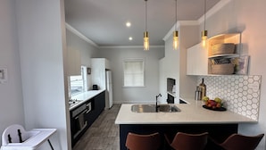 A modern kitchen with a central island, bar stools, pendant lights, and a built-in wine rack. - Pollyanna Hunter Valley (Cessnock)