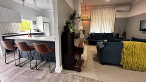 A modern kitchen with a central island, bar stools, a dining table, and a living area with a sofa and a coffee table. - Pollyanna Hunter Valley (Cessnock)