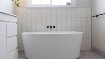 A modern bathroom with a freestanding bathtub, white tiled walls, and a window above the tub.