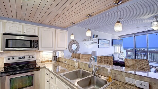 A modern kitchen with stainless steel appliances, a double sink, and a view of the balcony. - MP218 | Private Entry & Gulf Views | Resort Pools (Port Aransas)