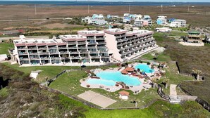 A large hotel with multiple balconies, a central swimming pool, and a surrounding grassy area. - MP218 | Private Entry & Gulf Views | Resort Pools (Port Aransas)