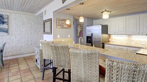 A kitchen with a wooden ceiling, white cabinets, a stainless steel refrigerator, and a woven chair. - MP218 | Private Entry & Gulf Views | Resort Pools (Port Aransas)