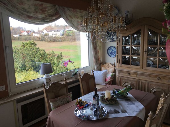 A dining room with a table set for two, a chandelier, and a view of the countryside.
