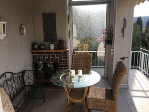 A balcony with a glass table and wicker chairs, a brick fireplace, and a view of trees and mountains.