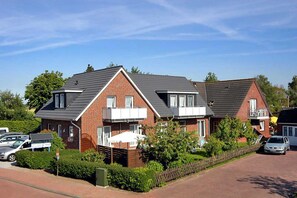 A row of two-story houses with brick exteriors and dark roofs, surrounded by greenery and a clear sky. - Vacation apartment Wadden Sea (1) - Holiday apartments in Haus Seekieker in Bensersiel (Esens)
