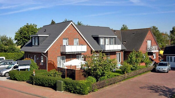 A row of two-story houses with brick exteriors and dark roofs, surrounded by greenery and a clear sky. - Vacation apartment Ebbe (3) - Holiday apartments in Haus Seekieker in Bensersiel (Esens)