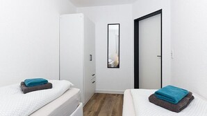A small, modern bedroom with two beds, a wooden floor, white walls, and a mirror on the wall. - Vacation apartment Ebbe (3) - Holiday apartments in Haus Seekieker in Bensersiel (Esens)
