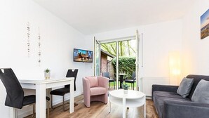 A modern living room with a white dining table, two chairs, a pink armchair, a gray sofa, and a white coffee table. - Vacation apartment Ebbe (3) - Holiday apartments in Haus Seekieker in Bensersiel (Esens)