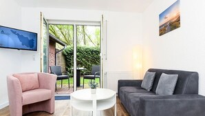 A living room with a grey sofa, a pink armchair, and a white coffee table. - Vacation apartment Ebbe (3) - Holiday apartments in Haus Seekieker in Bensersiel (Esens)