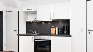 A compact kitchen with white cabinets, a black countertop, a built-in oven, and a coffee maker. - Vacation apartment Ebbe (3) - Holiday apartments in Haus Seekieker in Bensersiel (Esens)