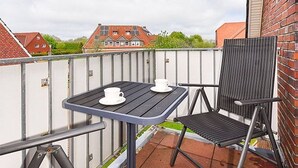 A balcony with a table and two chairs, a brick wall, and a view of houses in the background. - Vacation apartment Abendstern (5) - Holiday apartments in Haus Seekieker in Bensersiel (Esens)