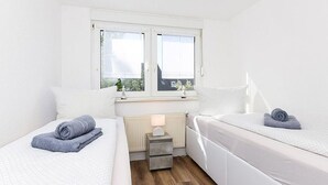A small, bright room with two beds, a radiator, and a window. - Vacation apartment Abendstern (5) - Holiday apartments in Haus Seekieker in Bensersiel (Esens)