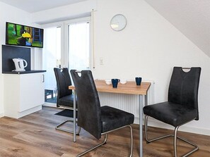 Una cocina moderna con televisor, dos sillas negras, una mesa de madera y un reloj en la pared.