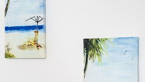 Two paintings of beach scenes with chairs and umbrellas.