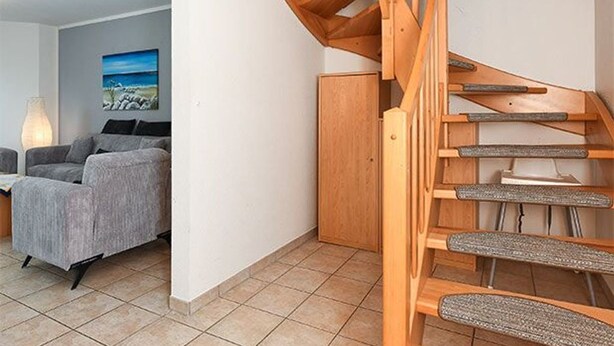 A wooden staircase in a room with a grey sofa and a painting on the wall.