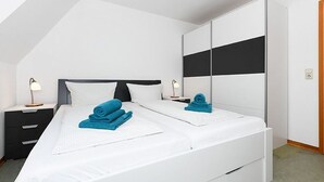 Een moderne slaapkamer met een wit bed, twee nachtkastjes en een grote kledingkast.