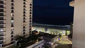 A high-rise hotel with multiple floors, a parking area, and a view of the beach at night.