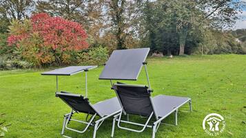 Two outdoor lounge chairs with attached sunshades in a grassy area with trees in the background.