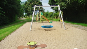 Une aire de jeux avec des balançoires, un toboggan et une structure d’escalade.