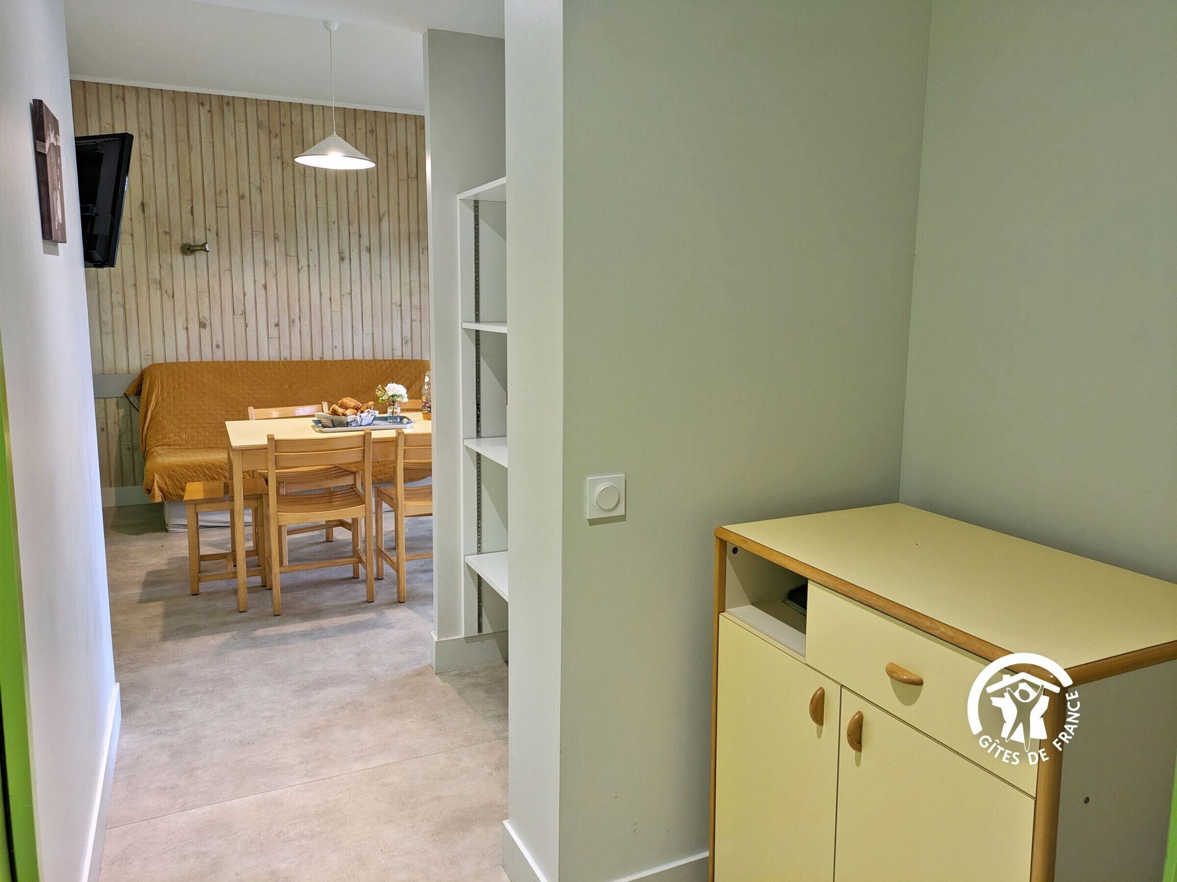A room with a bed, a dining table with chairs, a small kitchenette, and a wardrobe.