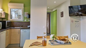 Une cuisine compacte avec une fenêtre, un four à micro-ondes et un lave-vaisselle. Une table à manger avec une bouteille et des pâtisseries se trouve au premier plan.