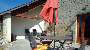 Un patio exterior con una mesa y sillas, una sombrilla roja y un edificio de piedra al fondo.