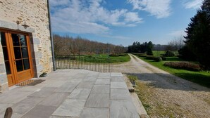 Un edificio de piedra con puerta de madera, un sendero empedrado y un camino de grava que conduce a un paisaje rural.