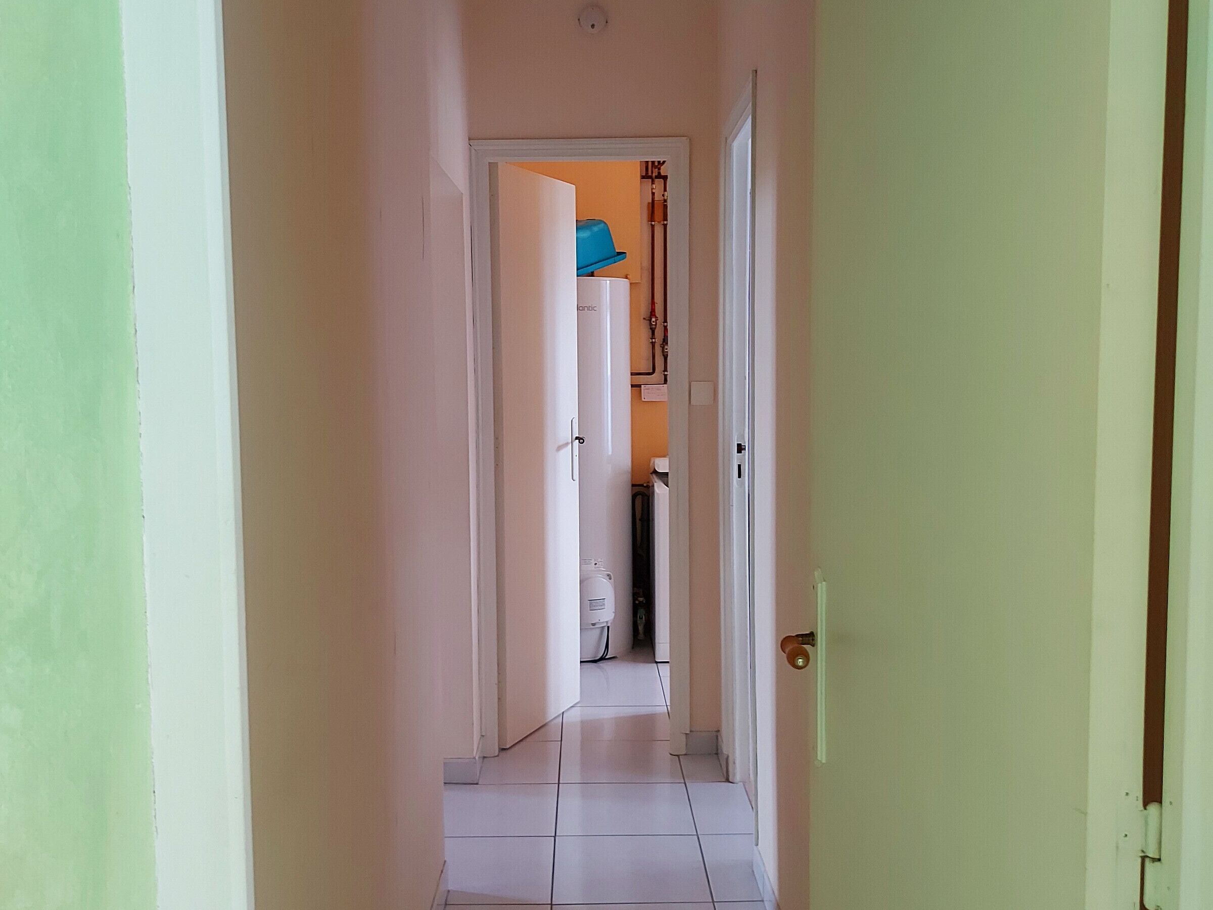 A narrow hallway with white tiled floors and light green walls.
