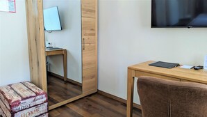 Ett rum med ett skrivbord i trä, en stol, en tv som är monterad på väggen och ett litet bord med en dator och ett tangentbord.