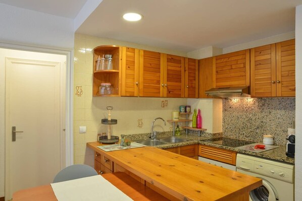 A compact kitchen with wooden cabinets, a granite countertop, and a built-in washing machine.