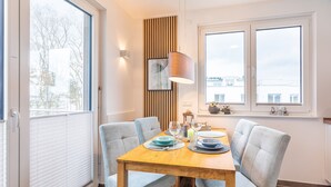 A dining area with a wooden table, four grey upholstered chairs, a hanging pendant light, and a window with blinds. - Apartment sun deck - Haffresidenz (4a.12) - 4a.12 (Zirchow)