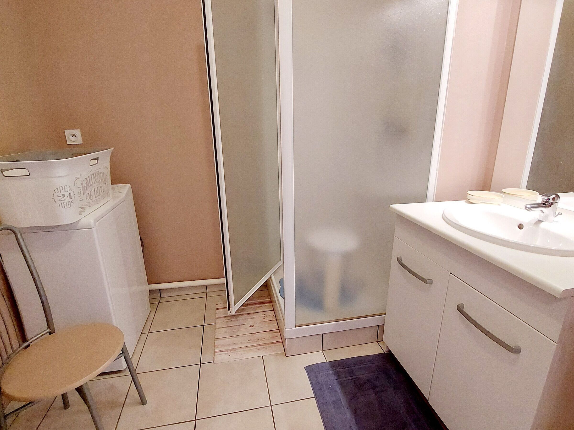 A bathroom with a shower, a sink, and a chair.