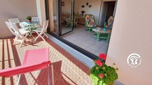 A balcony with a table and chairs, a sliding glass door leading to a dining area, and a potted plant. - Bright 2-Bedroom Apartment with Balcony, Garage & Baby Equipment near Mayenne's Attractions (Mayenne)