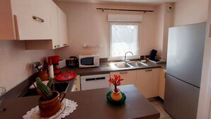 A compact kitchen with white cabinets, a microwave, a sink, and a refrigerator. - Bright 2-Bedroom Apartment with Balcony, Garage & Baby Equipment near Mayenne's Attractions (Mayenne)