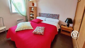 A bedroom with a bed, a nightstand, a lamp, a bookshelf, a chair, and a window with curtains. - Bright 2-Bedroom Apartment with Balcony, Garage & Baby Equipment near Mayenne's Attractions (Mayenne)