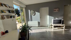 A living room with a television, a white door, a bookshelf, and a potted plant. - Riverside Retreat: Spacious 3BR House, Private Fishing Pond, Near Charming Villages & Outdoor Activities (Voutré)