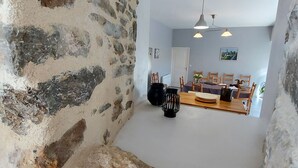 A dining area with a stone wall, wooden table, chairs, and hanging pendant lights. - Riverside Retreat: Spacious 3BR House, Private Fishing Pond, Near Charming Villages & Outdoor Activities (Voutré)
