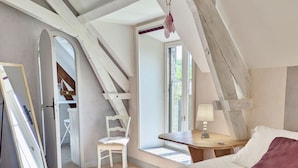 A bedroom with a large bed, a chair, a desk, and a window.